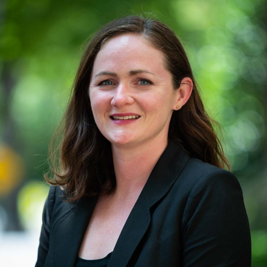 Image of a woman with dark brown hair smiling at the camera. She is wearing a black blouse and a black suit jacket.