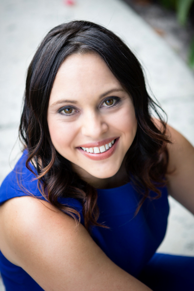 Image of a woman with black long hair smiling at the camera. She is wearing a blue dress.