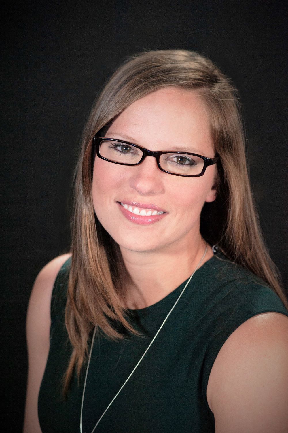 Image of a woman with brown hair wearing glasses and a black blouse, positioned in front of a black background.