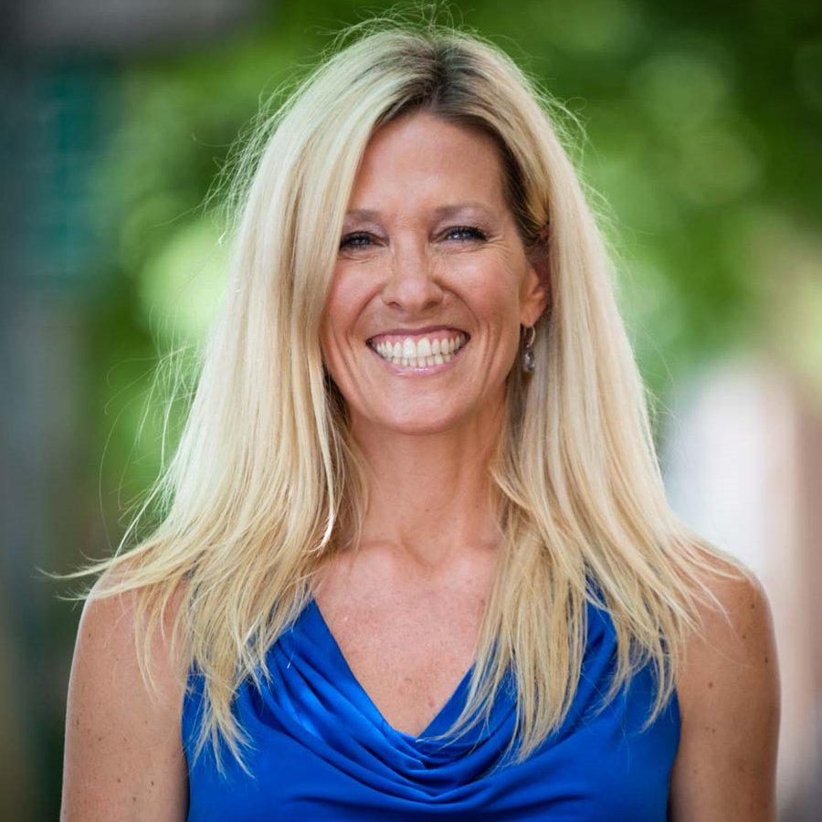 Image of a woman with long blonde hair smiling at the camera. She is wearing a bright blue sleeveless blouse.