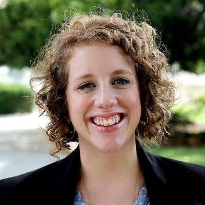 Headshot for Sarah Meek. Sarah has curly blonde hair and is wearing a black blazer.