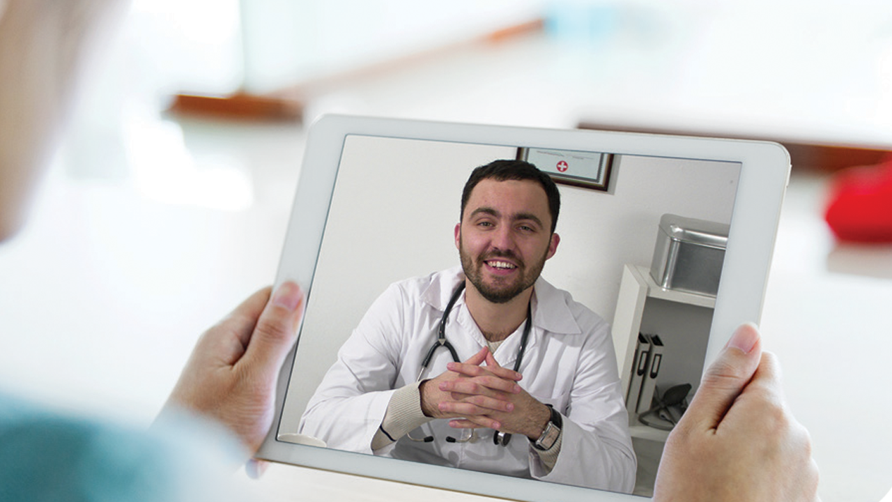 Person holding a tablet with a doctor on the screen with fingers interlocked and smiling