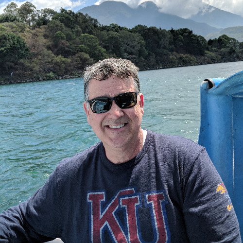 A photo of Mike Strouse on a boat in front of blue water and mountains in the background