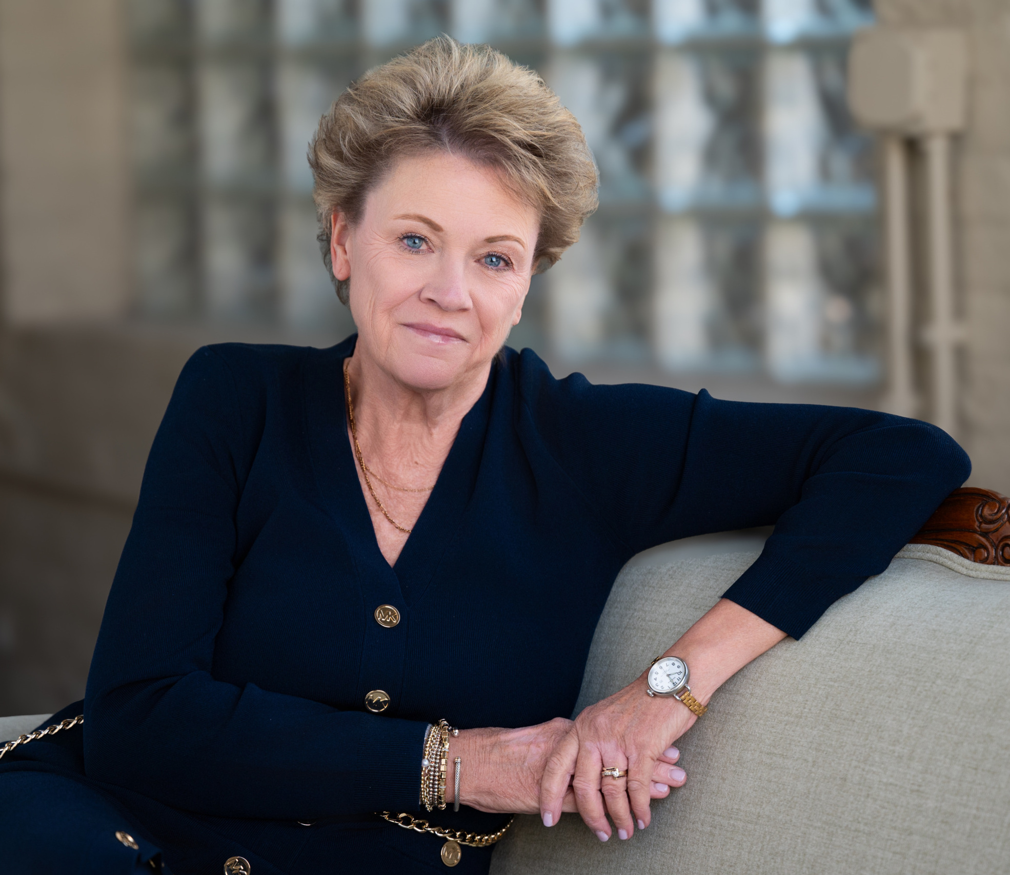 professional photo of Kathy Carmody, women sitting on couch with left elbow resting on the top and holding her right hand
