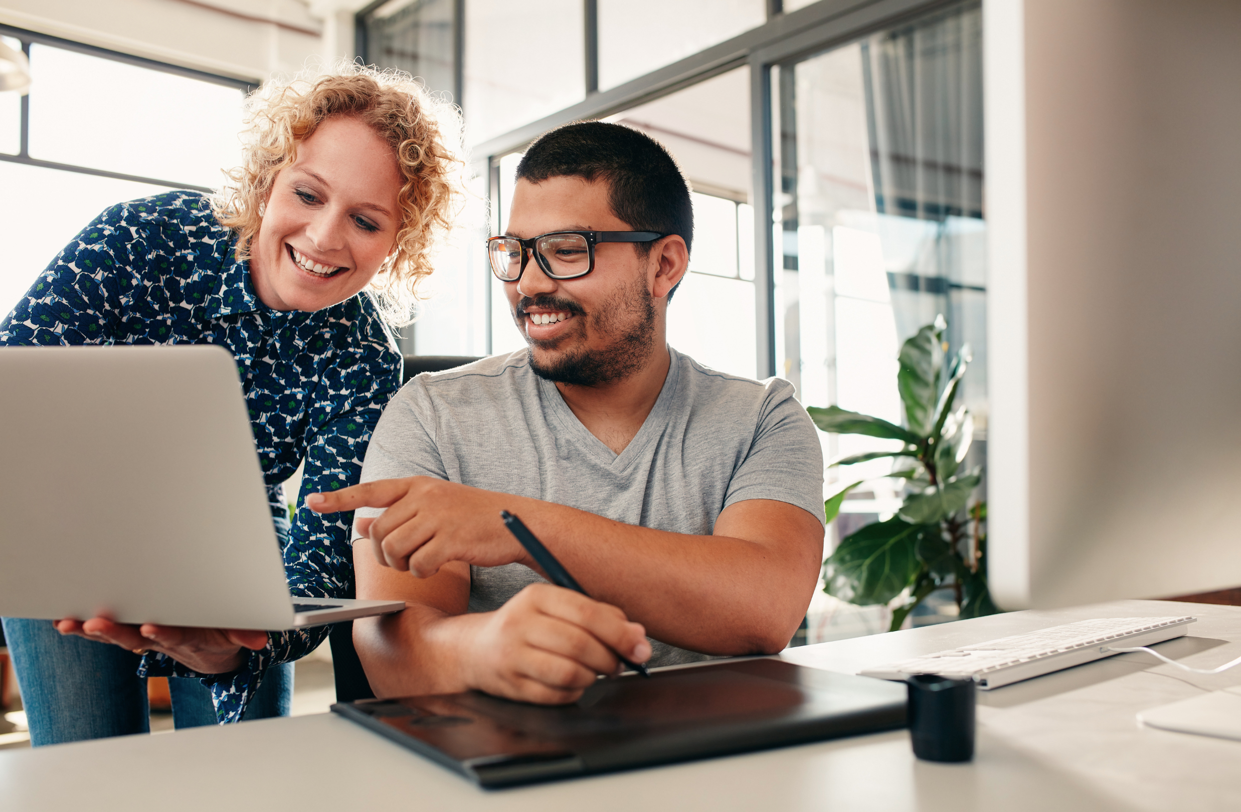 Stock photo of a young woman showing something on a laptop to a young man in an office setting