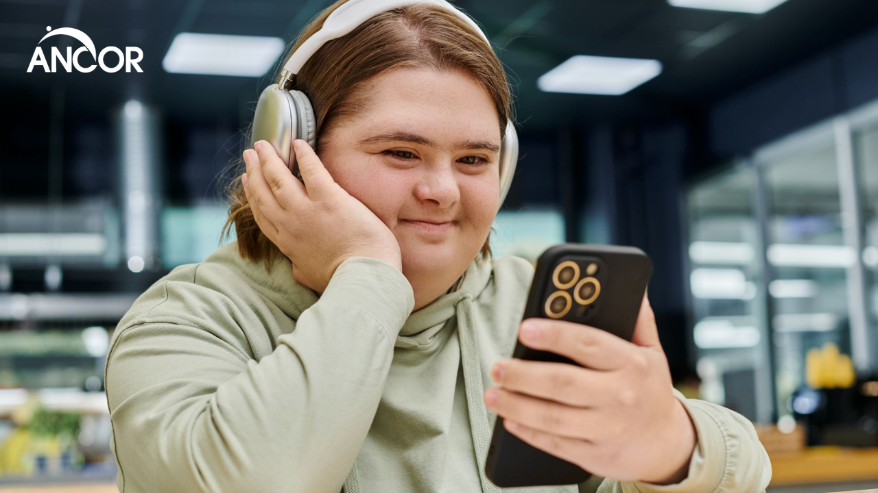 A person with intellectual disability wearing headphones and smiling at their smartphone