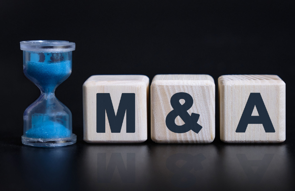 close up shot of three wooden blocks with 'M' '&' and 'A' on them, sitting next to an hourglass with blue sand