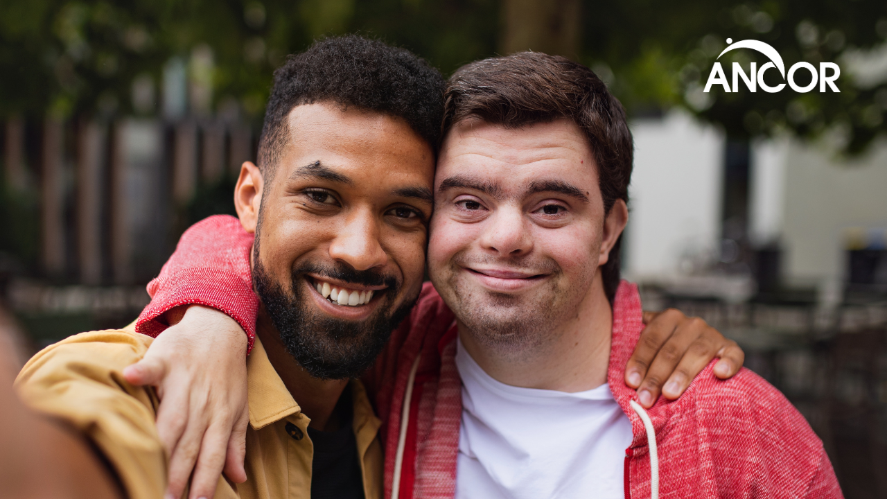 a person with I/DD smiling next to his support staff