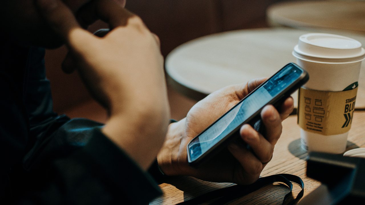 Stock photo of a person holding a smartphone with their coffee cup in the background
