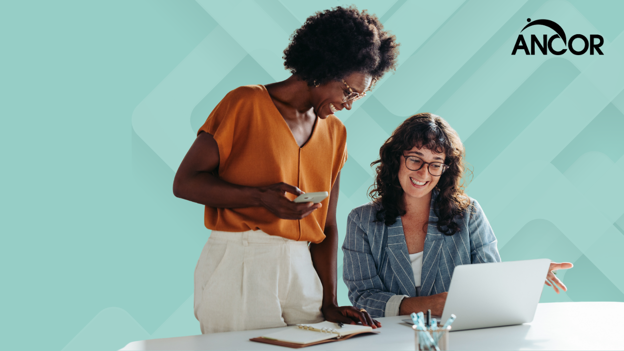 two coworkers, one older than the other, smiling and working together at a computer