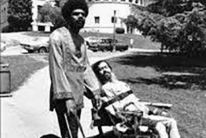 Activists Donald Galloway (left) and Ed Roberts (right). Galloway is standing and holding the handle of his guide dog’s harness, and Roberts is seated in a wheelchair.
