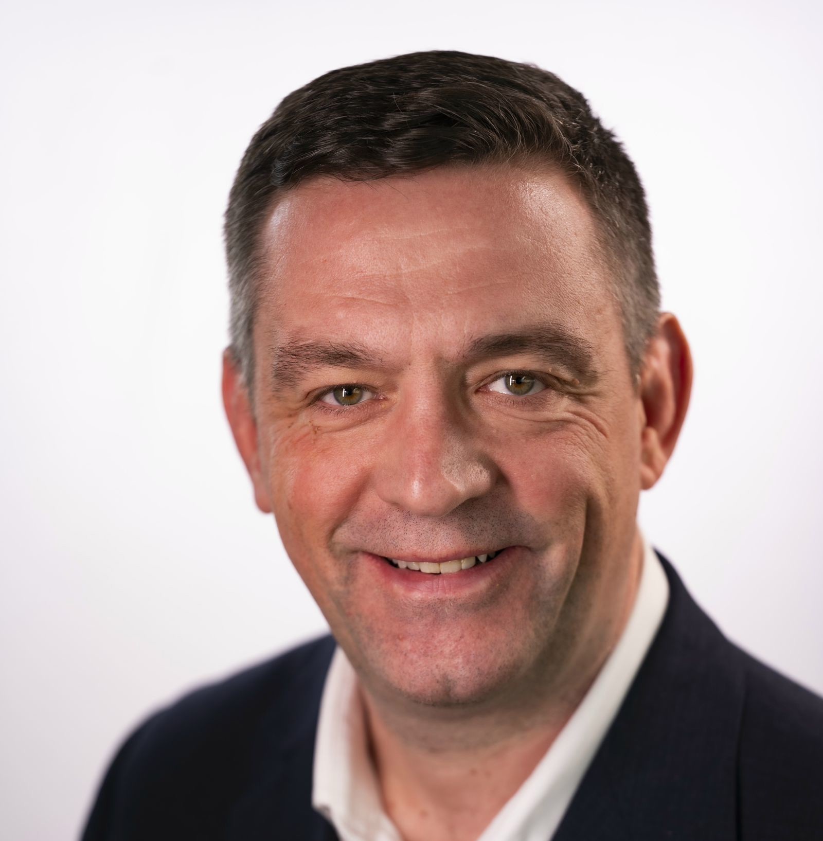A professional headshot of G. N. Janes, who has short brown hair and is wearing a dark sportcoat and a white, collared shirt.