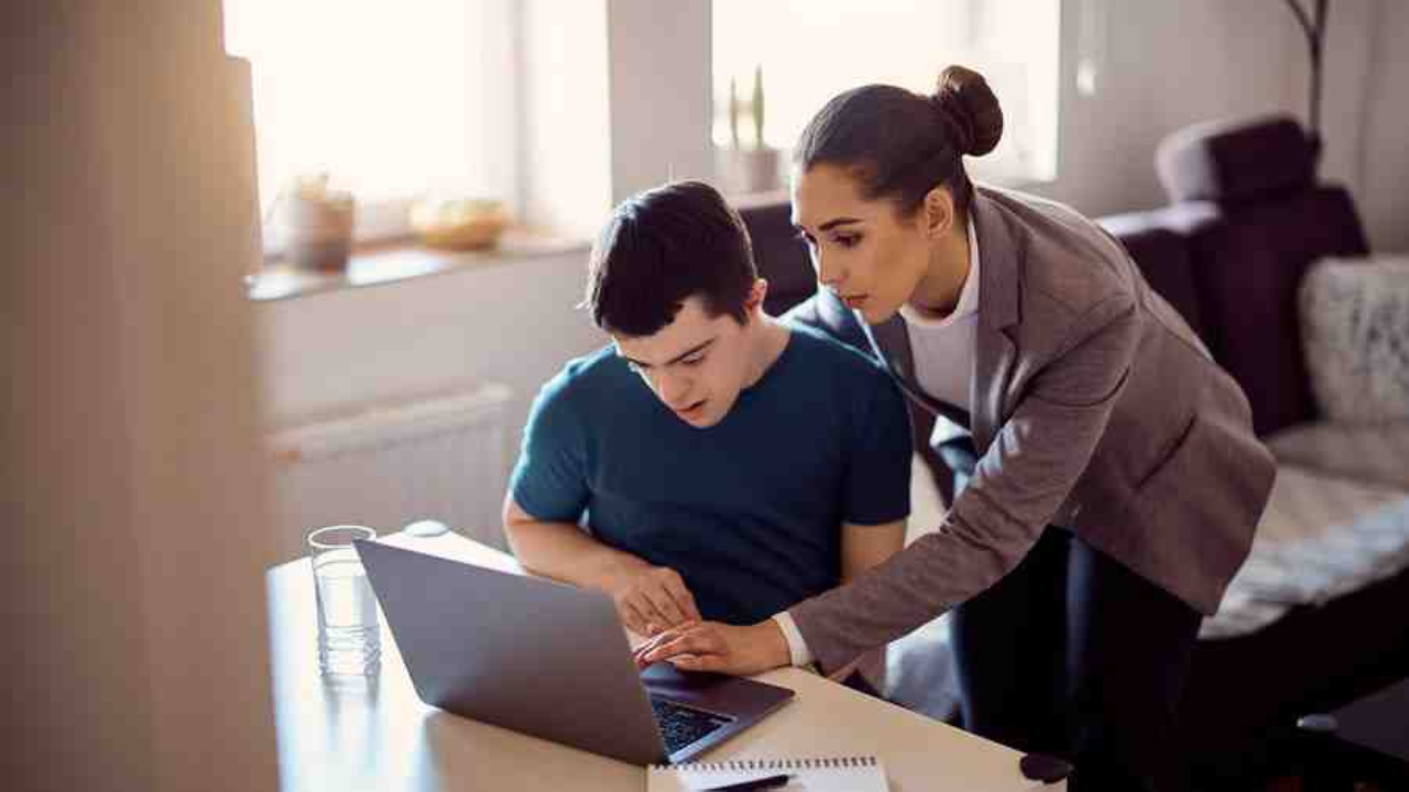 stock photo of a woman helping a person sitting in front of a laptop