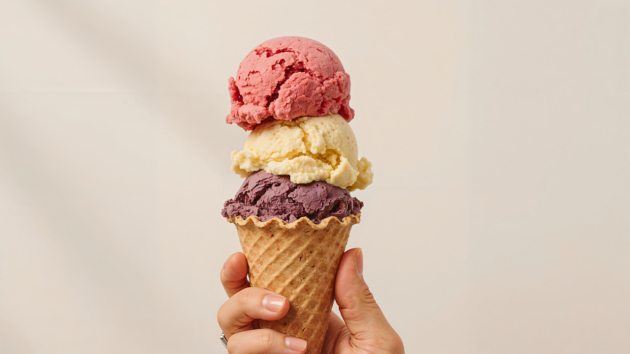 hand holding an ice cream cone with three scoops on top