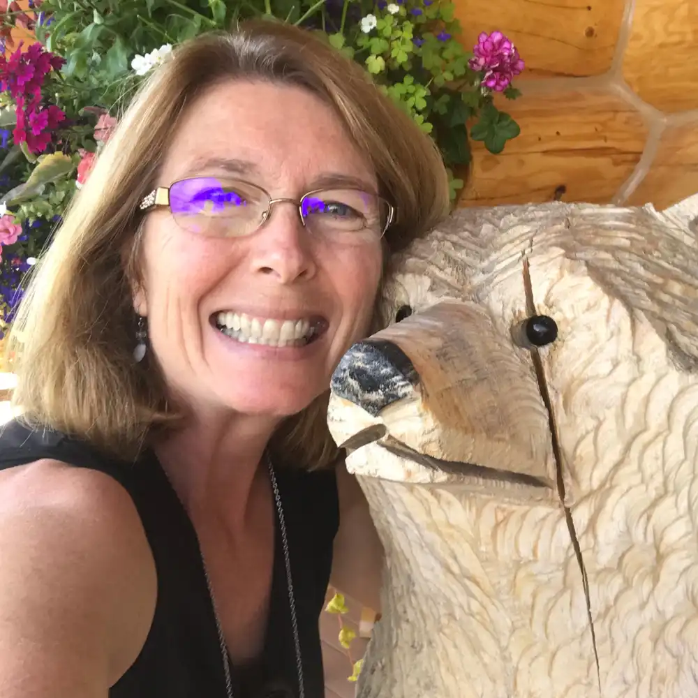 photo of Cindy Hensley smiling next to a dog carved from wood